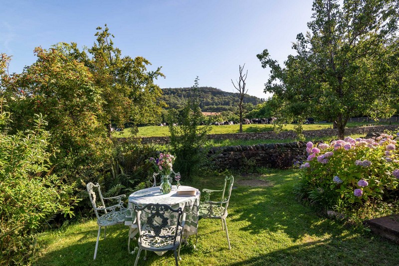 Garden furniture at side of holiday cottage in evening sun with book, wine and hydrangeas and a view to the Lake District fells
