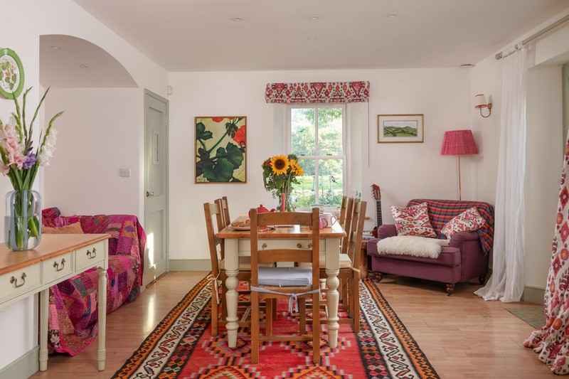 View of kitchen from middle, with bright art work, sumptuous armchair with sheepskin rug, lamp, wall lights and side table and sofa in alcove