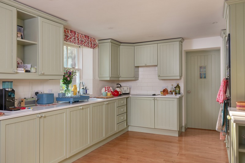 View of kitchen worktops with tea, flowers, blind, ovens and drying rack