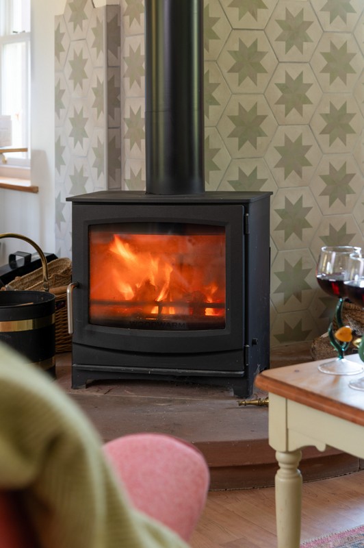 Lit fire with two glasses of red wine in unique, hand-made glasses and patterned tiles in the background