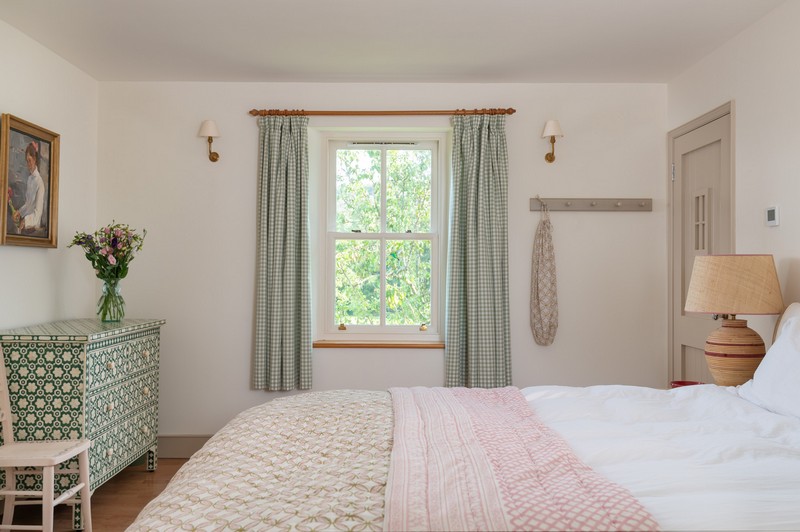 Main bedroom view of timber frame window, bedside lamp, wall lights and bed cover with flowers and painting