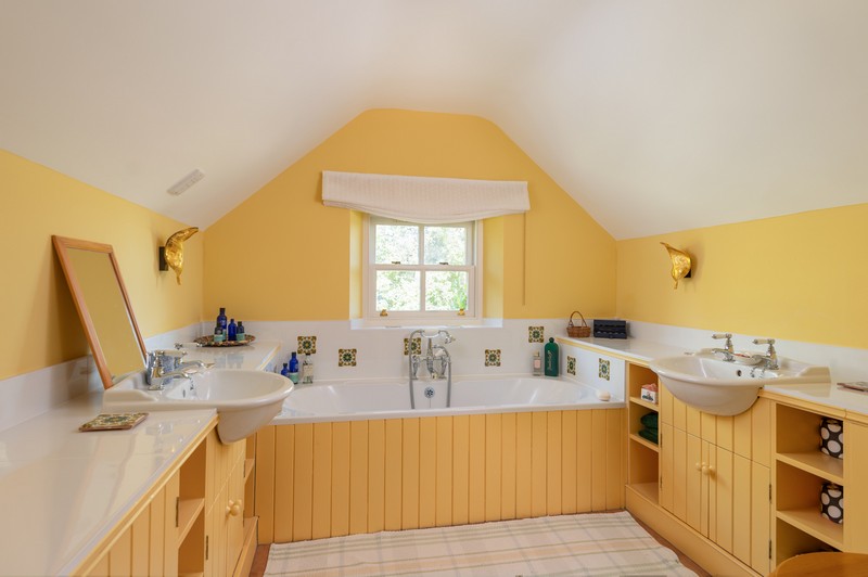 Yellow ensuite bathroom with golden leaf-shaped wall lamps and two sinks and deep bath