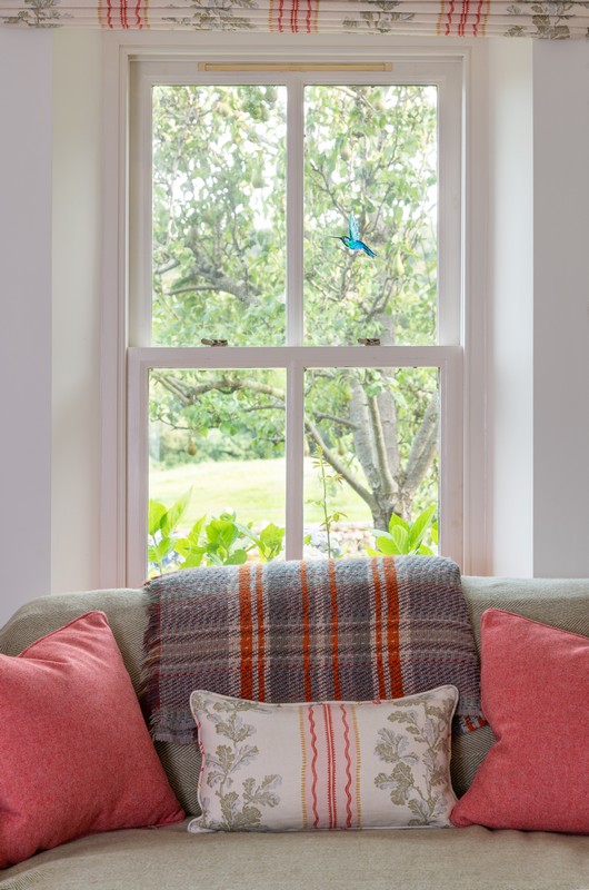 Timber sash window in drawing room with Linwood blind and cushions with recycled wool blanket on the sofa in drawing room