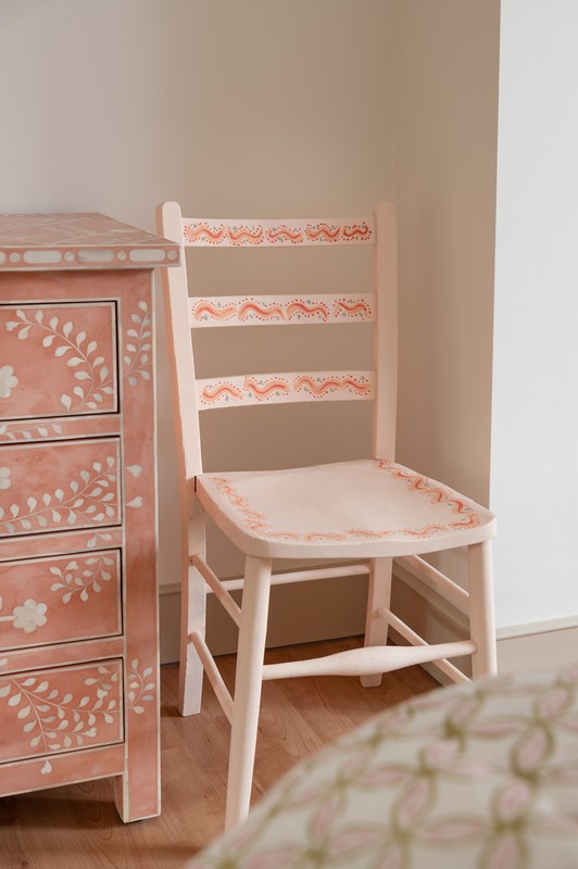 Hand-painted pink and orange chair next to mother of pearl pink chest of drawers in main bedroom