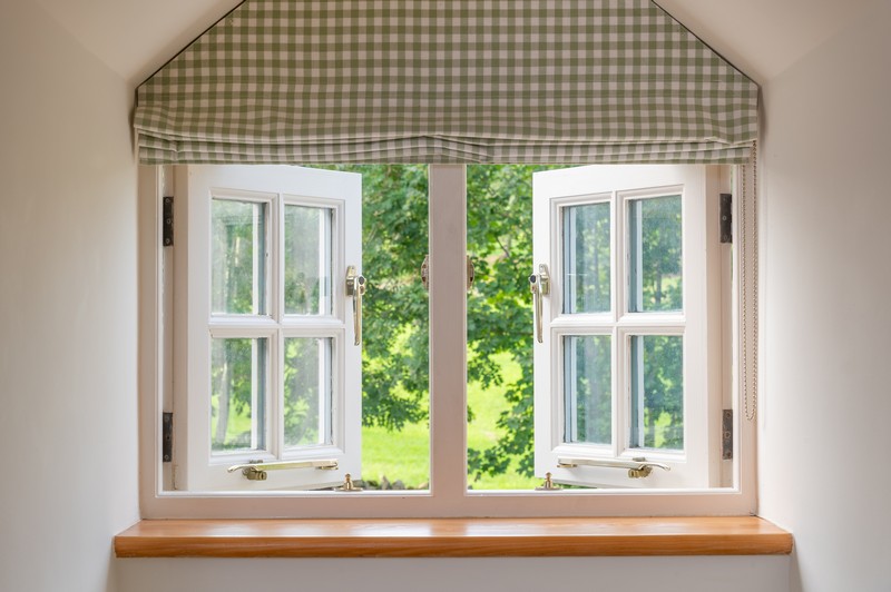 Green gingham blind in main bedroom with two open windows and wooden window ledge