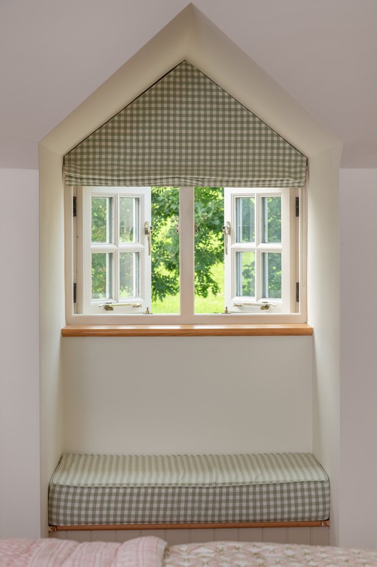Green gingham blind in main bedroom with two open windows, wooden window ledge and bay window cushioned seat also in green gingham