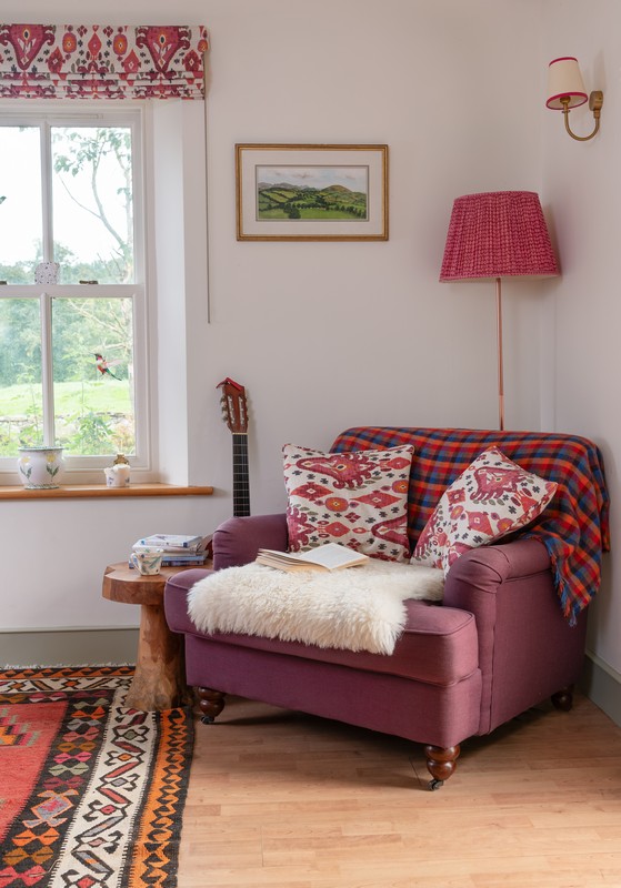 View of armchair in kitchen with brightly coloured cushions, sheepskin rug and blinds